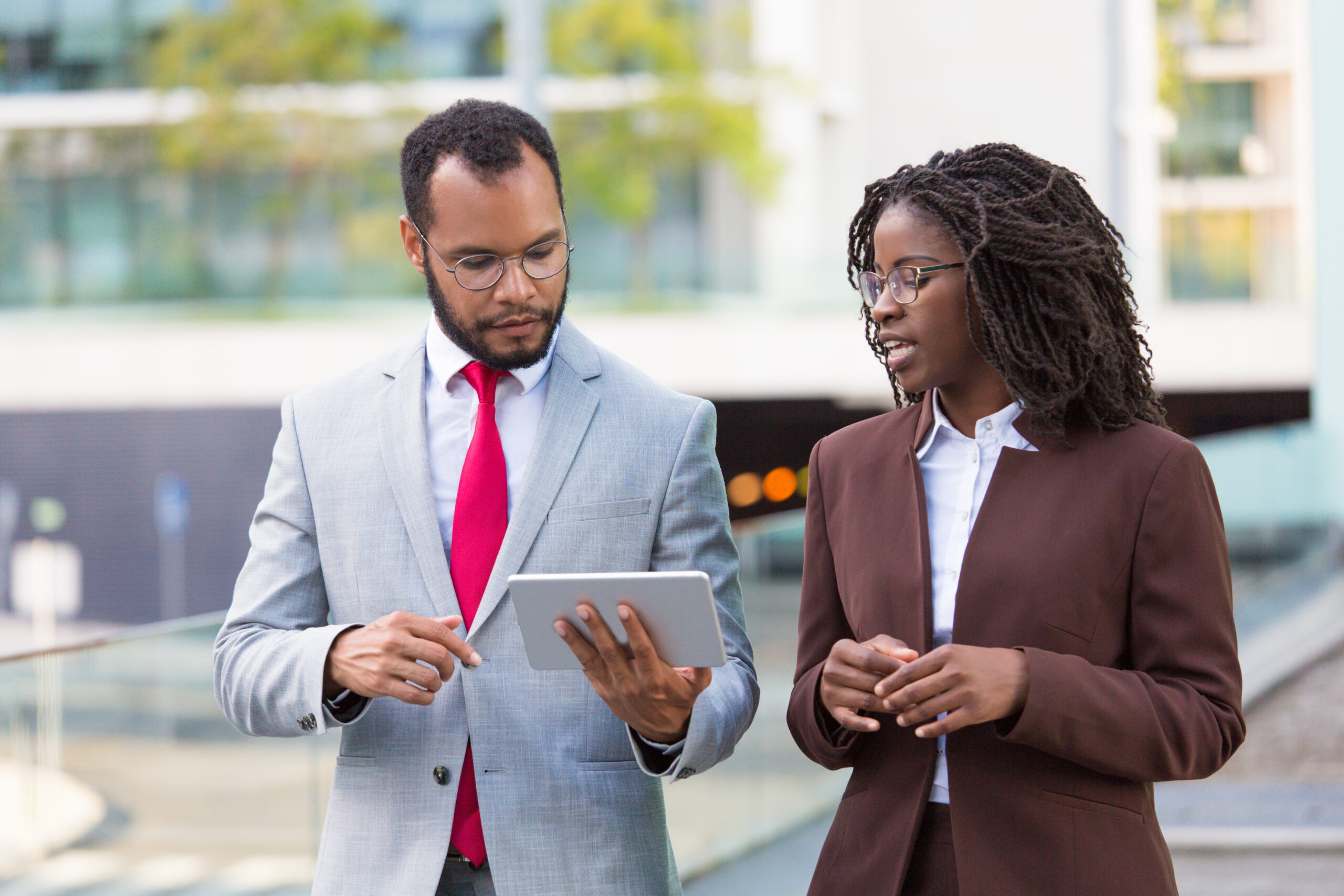 Multiethnic business team watching presentation on tablet on their way to office. Business man showing tablet screen to black female colleague while walking outdoors. Wi-Fi connection concept